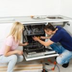 Young woman looking at repairman repairing dishwasher in kitchen