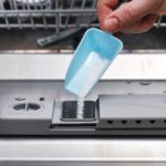 A man pours powder for washing dishes into dishwasher compartment.