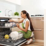 Beautiful young woman loading dishwasher in kitchen