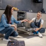 Woman holding out tool to plumbing near dishwasher
