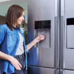 woman taking cold water into glass from home refrigerator